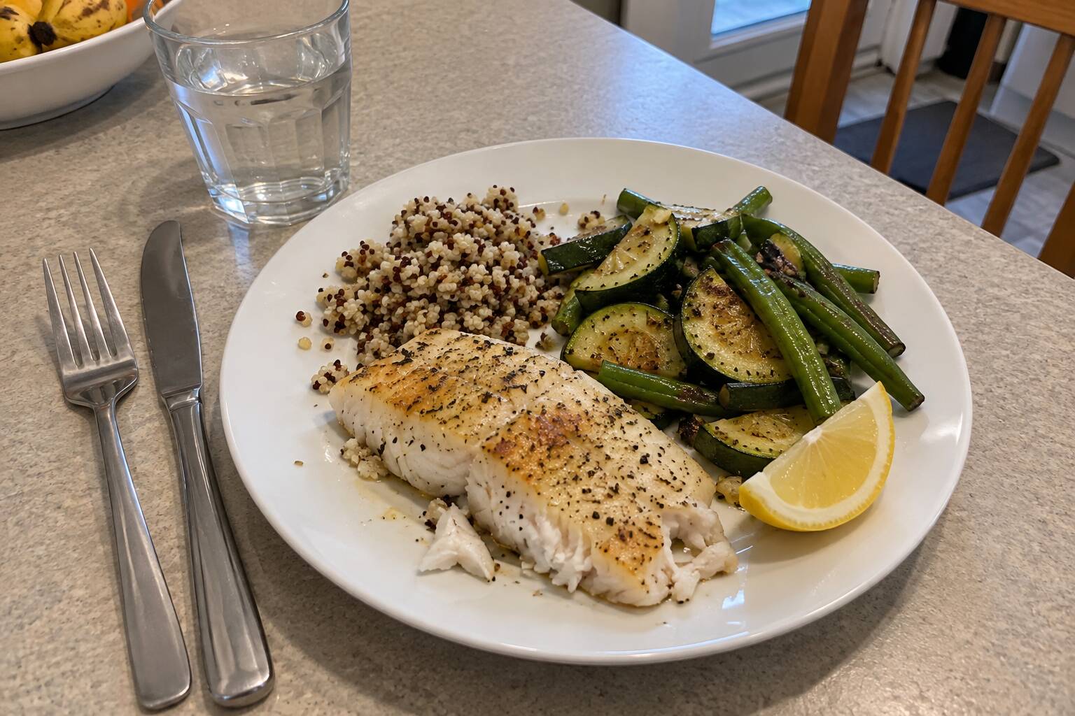 Une assiette contenant du poisson au four, du quinoa, des courgettes sautées